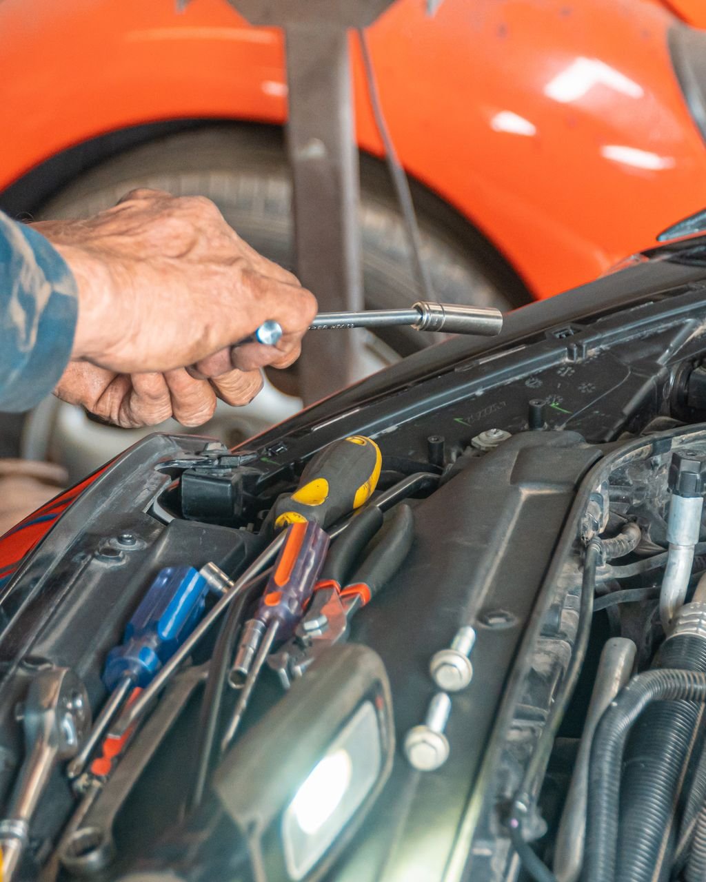 Mechanic's hand using a socket extension on the engine bay of a vehicle with the hood popped