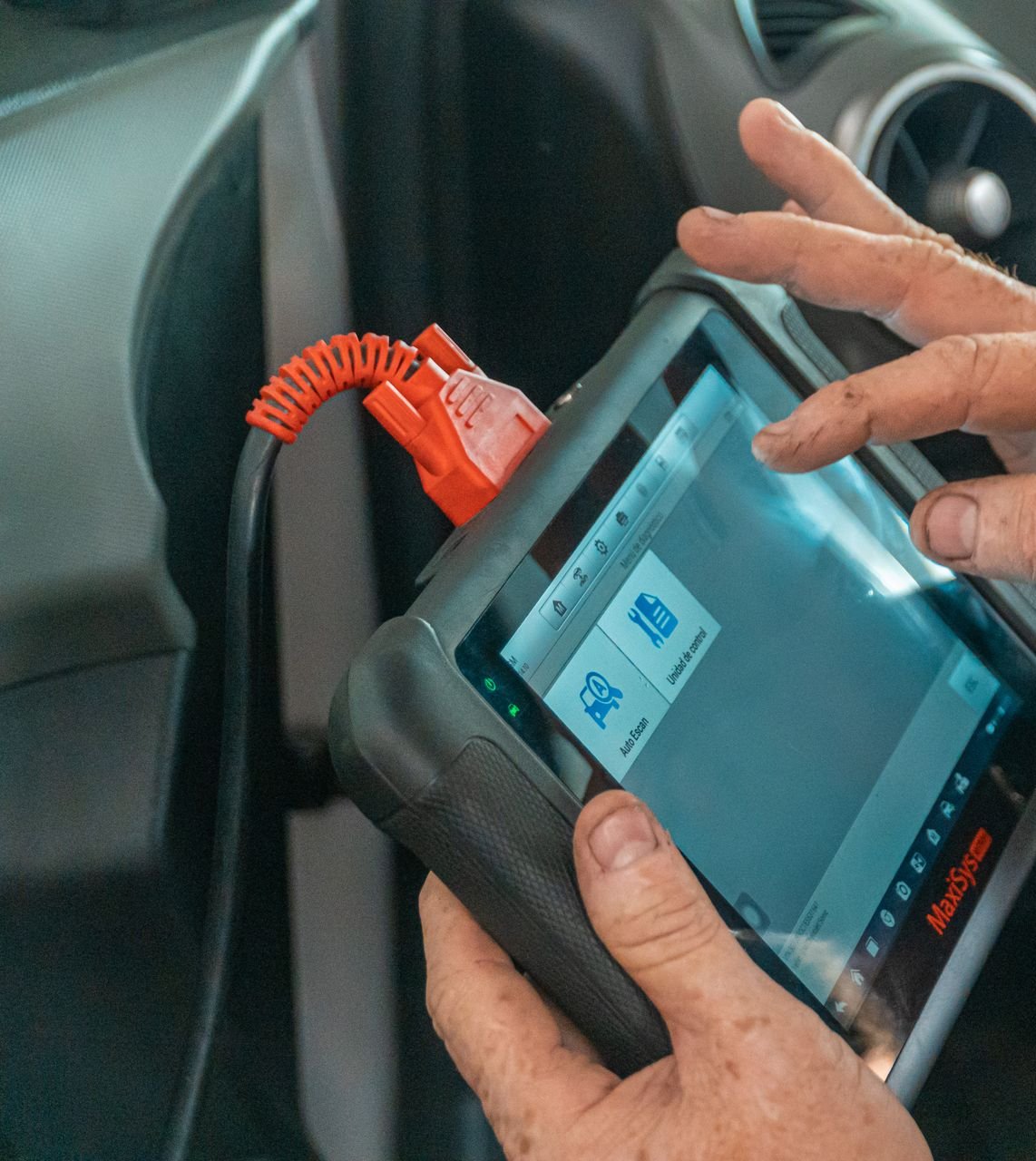 Hand holding a diagnostic scanner plugged into a vehicle's OBD port with a code readout on screen