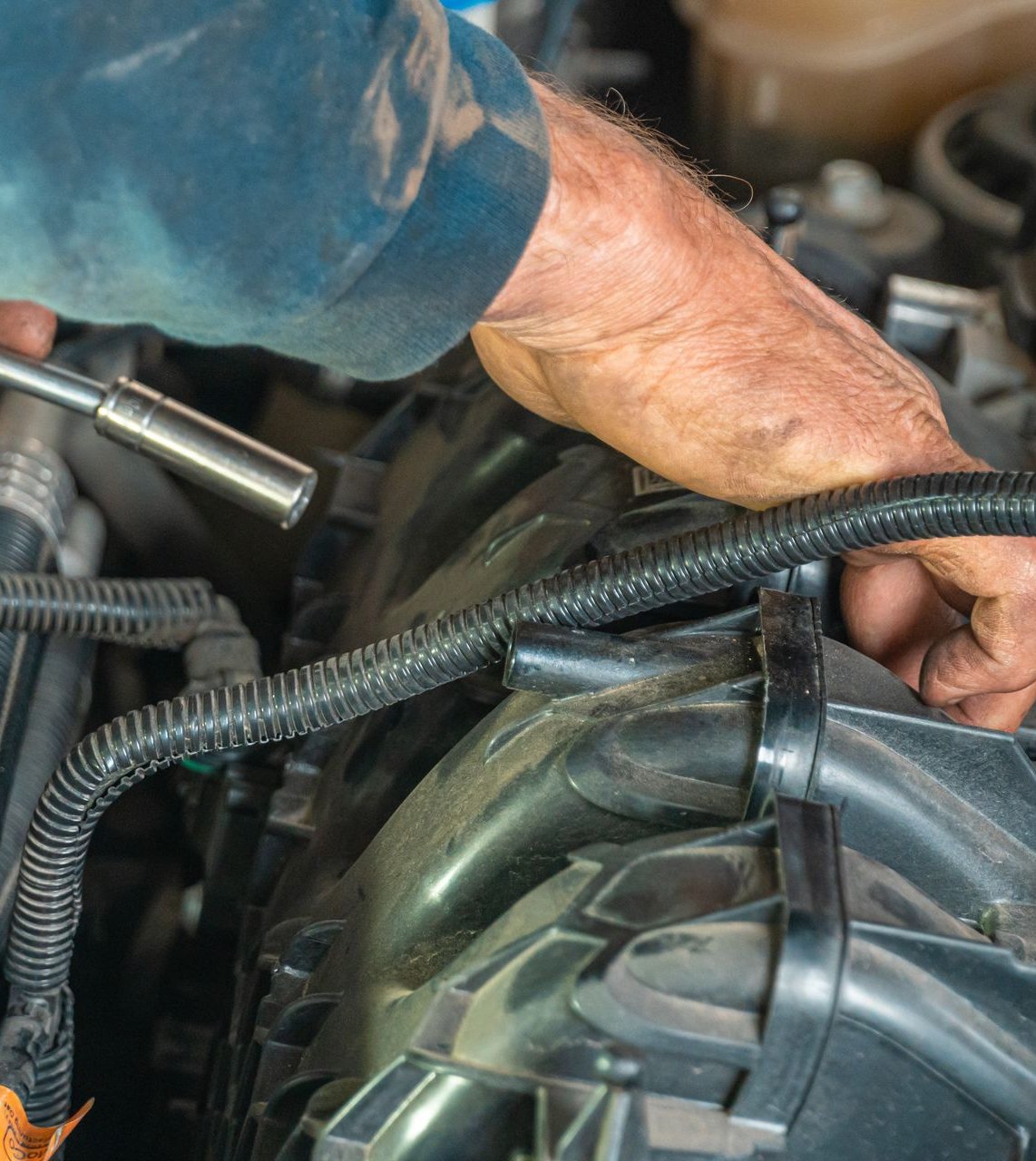 Mechanic's hand turning a socket wrench on an engine bay component under a popped hood